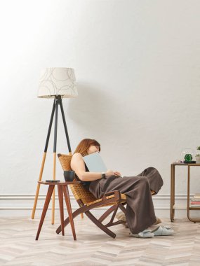 Bir kadın evde kitap okuyor, telefon ve tablete bakıyor. Bitkinin dekoratif iç stili ve vazosu.