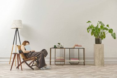 Bir kadın evde kitap okuyor, telefon ve tablete bakıyor. Bitkinin dekoratif iç stili ve vazosu.