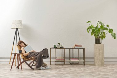 Bir kadın evde kitap okuyor, telefon ve tablete bakıyor. Bitkinin dekoratif iç stili ve vazosu.