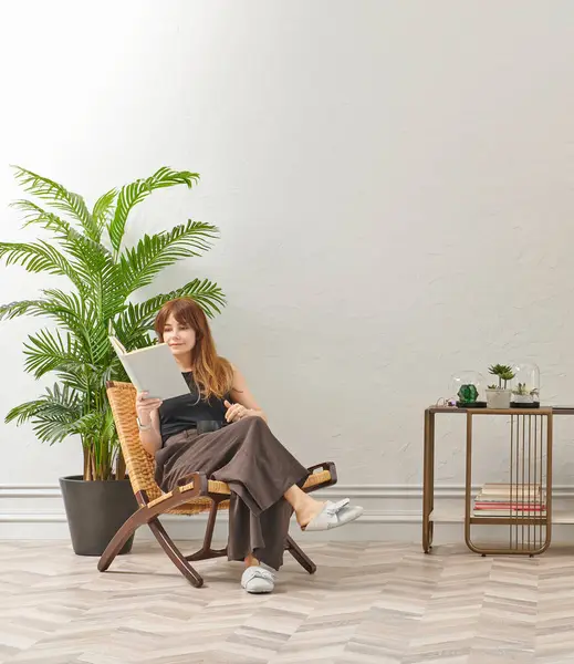 Bir kadın evde kitap okuyor, telefon ve tablete bakıyor. Bitkinin dekoratif iç stili ve vazosu.