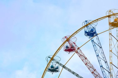 Multi colored ferris wheel and blue sky in a light cloudy haze