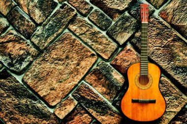 Gri kahverengi tuğla duvarda sarı turuncu akustik gitar