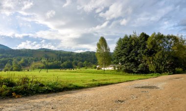 Dağlık bir bölgede yeşil bir otlağın yanındaki kırsal toprak yol.                               