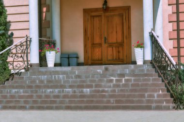 Geniş merdiven ve binanın girişi. Sütunları ve ahşap bir kapısı var.                               