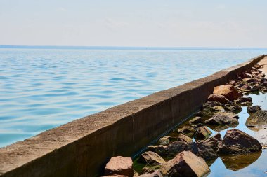 Koruyucu beton kıyı iskelesi dalgakıranı, ılık güneşli havada mavi su                               