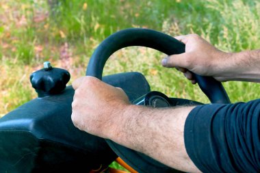 Male hands of the driver holding the steering wheel of a tractor, lawn mower                               