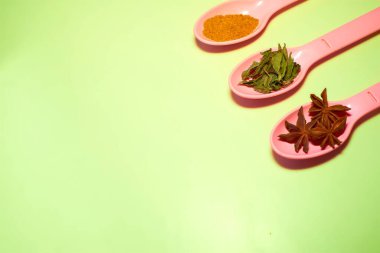 Pink spoons with spices for cooking on a green surface