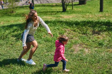 Genç bir anne çocuğunu yeşil çimlerde oynarken yakalar.                               