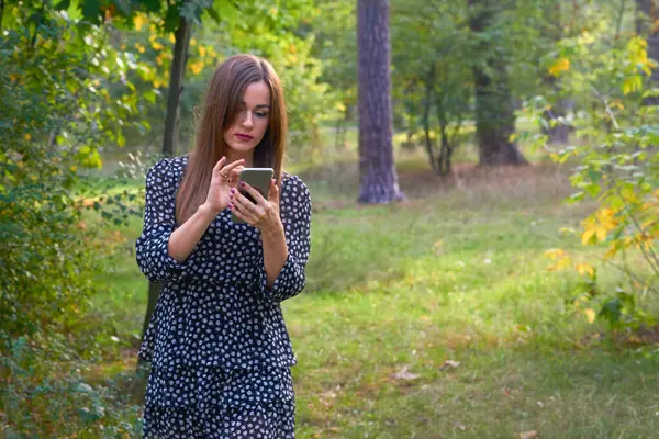 Pretty woman writes a message, looks at the phone, trees in a forest park