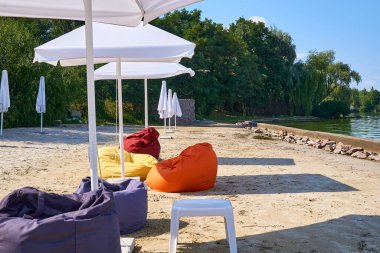 Deniz kenarında kapalı şemsiyeleri ve beyaz bir köpeği olan terk edilmiş kumlu bir sahil.                               