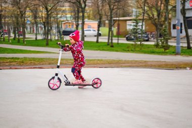 Neşeli aktif çocuk şehir parkında pembe bir scooter sürüyor.                               