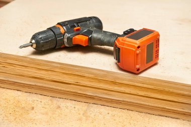 Electric drill,screwdriver on a plywood wooden surface with sawdust in workshop                               