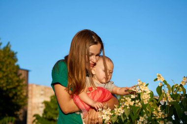 Genç mutlu anne, güzel kızıyla parkta bir çocukla yürüyor.