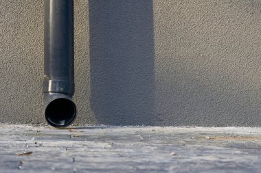 Yağmur damlaları. Gri alçılı duvarda yeni bir plastik boru.