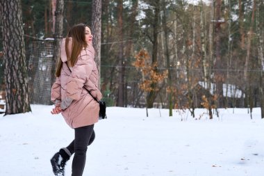 Pembe ceketli bir kadın kış parkında yürüyor.