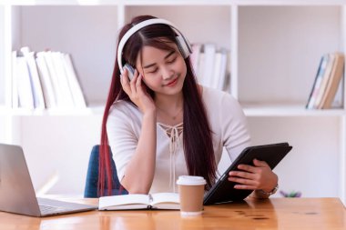 Asyalı kadınlar kulaklık takarlar müzik dinlerler gevşeyip dijital tablet kullanırlar. İnternetten öğrenen güzel bir kadın. Kulaklık takar ve çalışır..
