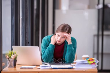 İş kadınları, ofiste dizüstü bilgisayar ve kağıt belgeler önünde çalışmakla strese girerler. İş konsepti.