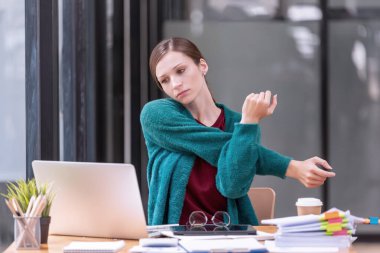 Genç işkadını ofis çalışanı tembelce esneyerek ofis masasının çalışma yerindeki acıyı hafifletiyor, kendini çok yorgun hissediyor. Ofis sendromu.