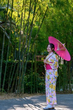 Geleneksel Japon kimonosu ya da şemsiyesi olan genç bir kadın parkta mutlu ve neşelidir. Japon geleneksel yaz elbisesi.