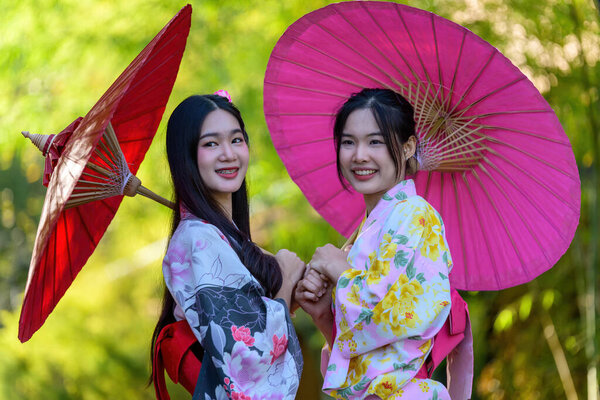 A young woman wearing a Japanese traditional kimono or yukata holding an umbrella is happy and cheerful in the park. Japanese traditional summer dress.