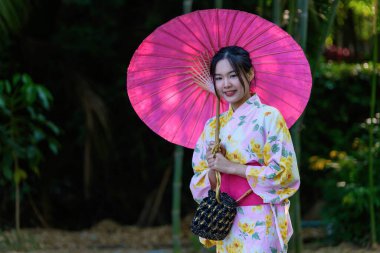 Geleneksel Japon kimonosu ya da şemsiyesi olan genç bir kadın parkta mutlu ve neşelidir. Japon geleneksel yaz elbisesi.