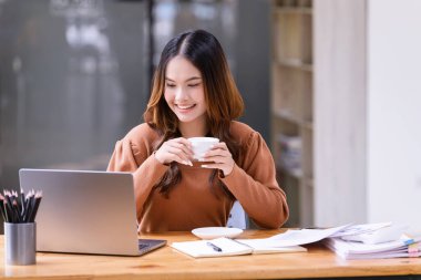 Ofisteki çalışma masasında oturan bir fincan kahve içen genç bir kadın. İş gündelik konsepti