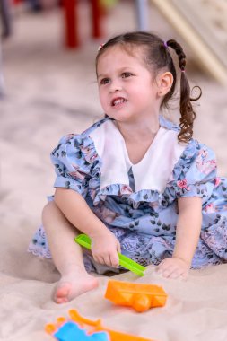 Oyun sahasında kumlarda oynayan tatlı bir kız. Çocukların oyun parkında eğlenmesi kavramı