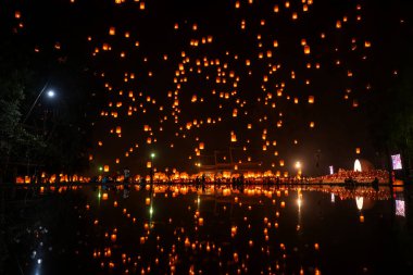 Gökyüzüne yükselen ateş fenerleri, Tayland 'ın Chiang Mai şehrinin seyahat bayramında gece sudaki yansımalarıdır. Gece vakti Chiang Mai, Tayland 'daki Yee Peng Festivali' nde gökyüzü fenerinin arka planı.
