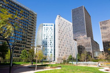Güneşli bir günde çevresi yeşil ağaçlar ve çimlerle çevrili modern ofis binalarıyla dolu bir iş bölgesi.
