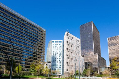 Güneşli bir günde çevresi yeşil ağaçlar ve çimlerle çevrili modern ofis binalarıyla dolu bir iş bölgesi.