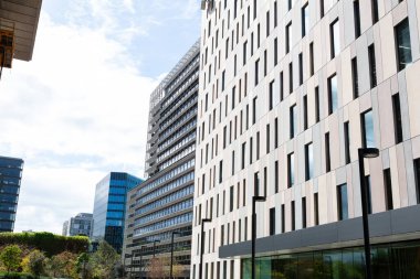 Güneşli bir günde çevresi yeşil ağaçlar ve çimlerle çevrili modern ofis binalarıyla dolu bir iş bölgesi.