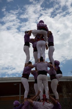Geleneksel beyaz pantolon ve mor gömlekler giyen Katalan halkı, yerel festivaller için bir insan kulesi, bir castell inşa ediyorlar.