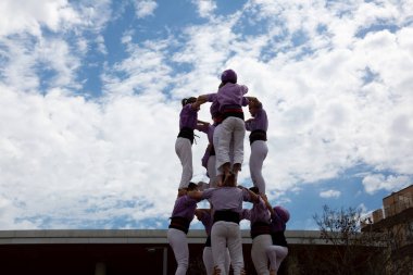 Geleneksel beyaz pantolon ve mor gömlekler giyen Katalan halkı, yerel festivaller için bir insan kulesi, bir castell inşa ediyorlar.