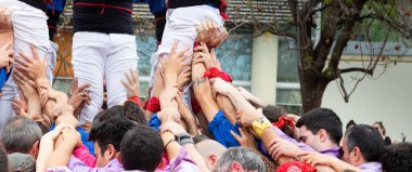 Geleneksel beyaz pantolon ve mor gömlekler giyen Katalan halkı, yerel festivaller için bir insan kulesi, bir castell inşa ediyorlar.