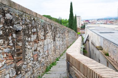 Turistler güneşli bir günün tadını çıkarırken Girona şehrini çevreleyen antik taş bir duvarın üzerinde yürüyorlar.