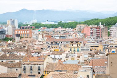Katalonya 'da bulutlu bir günde geleneksel terracotta çatılarını ve uzak dağları gösteren Girona şehri manzarası