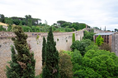 Turistler güneşli bir günün tadını çıkarırken Girona şehrini çevreleyen antik taş bir duvarın üzerinde yürüyorlar.