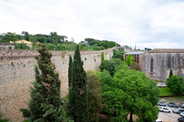 Turistler güneşli bir günün tadını çıkarırken Girona şehrini çevreleyen antik taş bir duvarın üzerinde yürüyorlar.