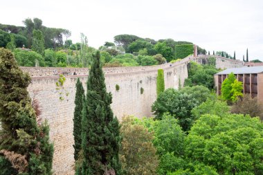 Turistler güneşli bir günün tadını çıkarırken Girona şehrini çevreleyen antik taş bir duvarın üzerinde yürüyorlar.