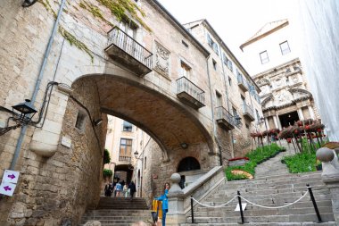 Girona 'nın eski kasabasında merdivenlerden çıkan turistler kemerli ve arka planda bir kilise var.