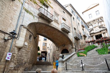 Girona 'nın eski kasabasında merdivenlerden çıkan turistler kemerli ve arka planda bir kilise var.