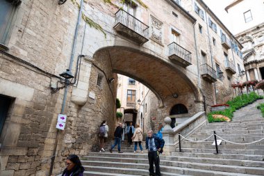 Girona 'nın eski kasabasında merdivenlerden çıkan turistler kemerli ve arka planda bir kilise var.