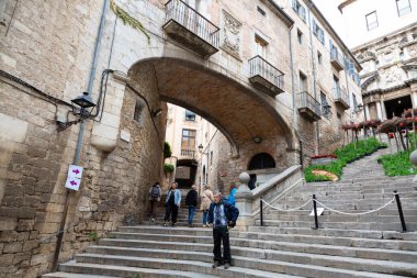 Girona 'nın eski kasabasında merdivenlerden çıkan turistler kemerli ve arka planda bir kilise var.