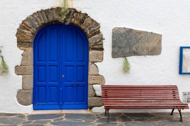 Önünde taş kemerli parlak mavi bir kapı ve önünde beyaz bir bina var.