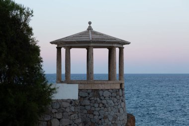 Uçuruma tünemiş taştan bir taraçanın sakin manzarası. Güneş batarken denizin engin genişliğine bakıyor.