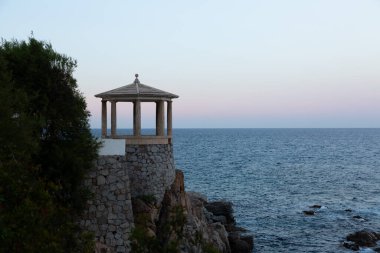 Uçuruma tünemiş taştan bir taraçanın sakin manzarası. Güneş batarken denizin engin genişliğine bakıyor.