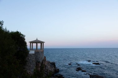 Uçuruma tünemiş taştan bir taraçanın sakin manzarası. Güneş batarken denizin engin genişliğine bakıyor.