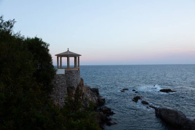 Uçuruma tünemiş taştan bir taraçanın sakin manzarası. Güneş batarken denizin engin genişliğine bakıyor.