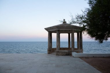 Uçuruma tünemiş taştan bir taraçanın sakin manzarası. Güneş batarken denizin engin genişliğine bakıyor.