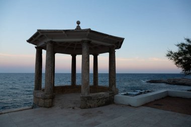 Uçuruma tünemiş taştan bir taraçanın sakin manzarası. Güneş batarken denizin engin genişliğine bakıyor.